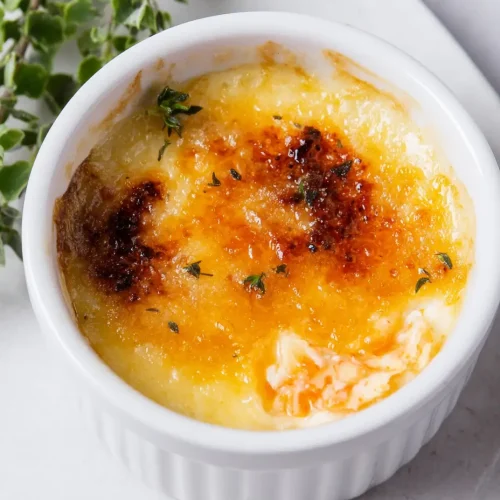 A close-up of crab brûlée in a white ramekin with a caramelized top and herb garnish.