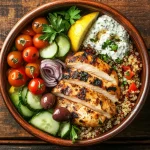 Grilled chicken Mediterranean bowl with quinoa, cherry tomatoes, tzatziki sauce, cucumbers, olives, and fresh herbs.
