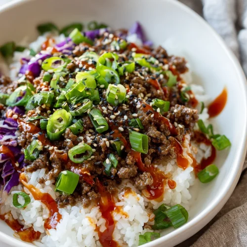 Korean ground beef bowl with rice, shredded purple cabbage, sesame seeds, green onions, and spicy sauce drizzle.