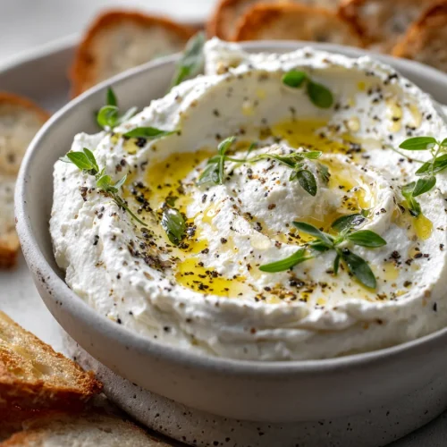 Creamy whipped ricotta dip topped with olive oil, fresh thyme, and cracked black pepper with toasted bread slices