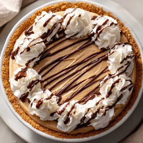 Creamy easy peanut butter pie topped with whipped cream swirls and chocolate drizzle on graham cracker crust
