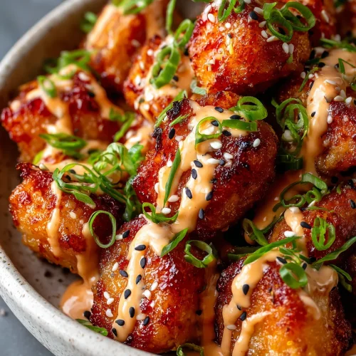Bang bang salmon bites drizzled with creamy sauce and topped with green onions and sesame seeds in a bowl