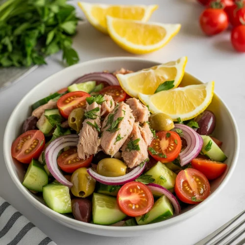 Mediterranean tuna salad with cucumbers, cherry tomatoes, olives, red onion, and lemon wedges