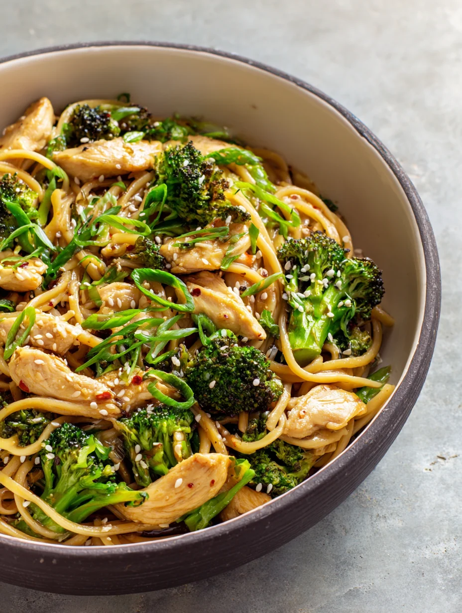 Spicy garlic chicken and broccoli noodle bowl topped with sesame seeds and green onions