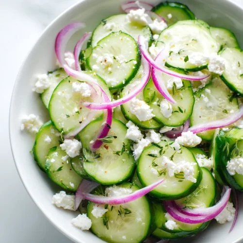 Cucumber feta salad with red onions and herbs in a light dressing, served in a bowl.