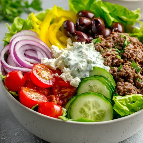 Mediterranean burger bowl with ground beef, cucumbers, cherry tomatoes, olives, feta cheese, and tzatziki.