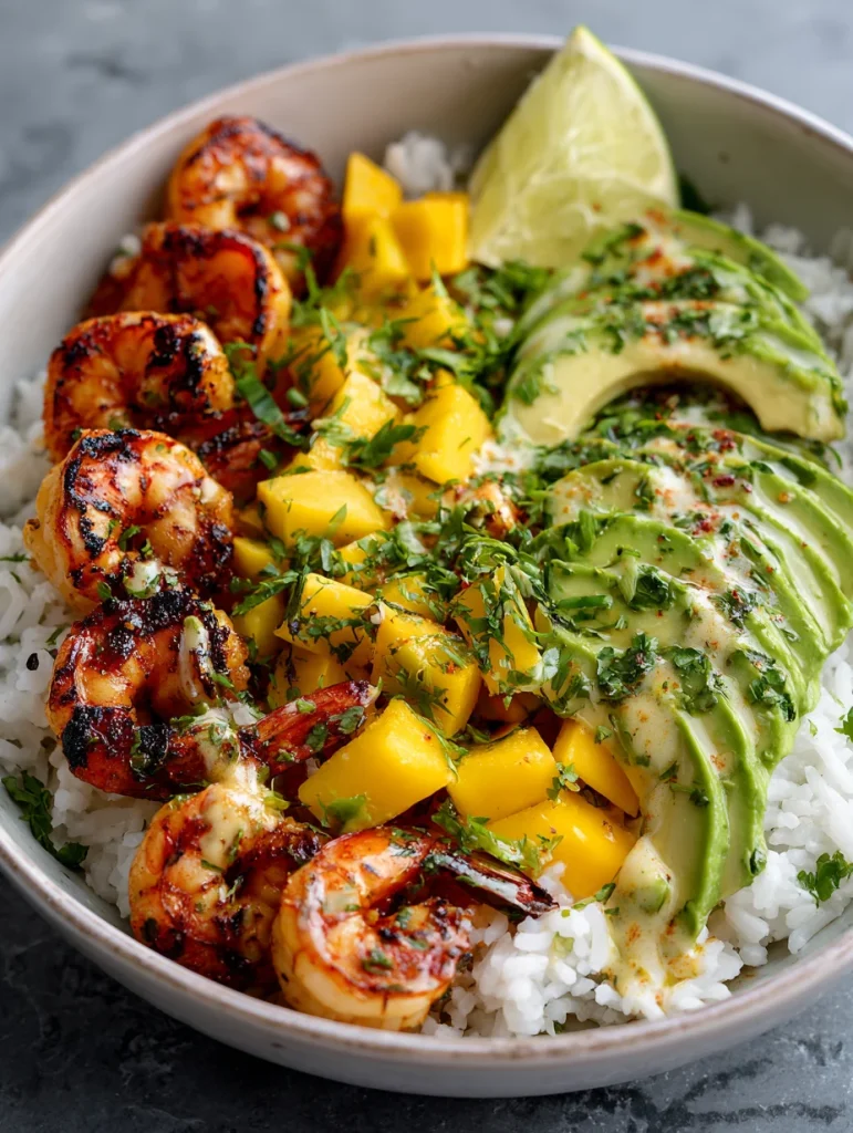 Shrimp mango rice bowl with grilled shrimp, avocado slices, mango chunks, and lime over white rice.