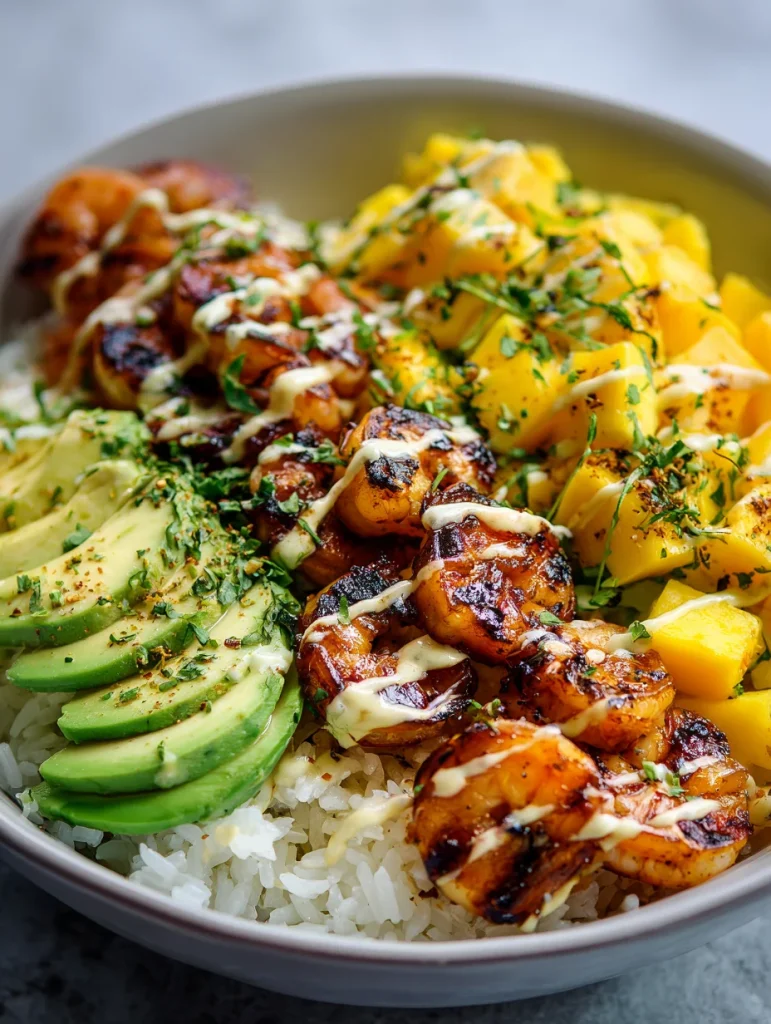 Shrimp mango rice bowl with grilled shrimp, avocado slices, mango chunks, and creamy sauce over white rice.