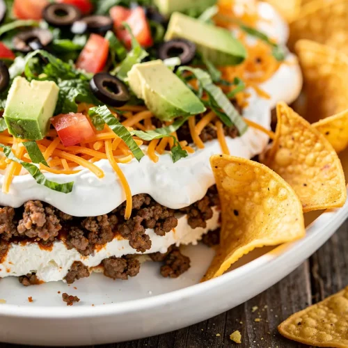 Close-up of layered taco dip with cream cheese, beef, avocado, and tortilla chips